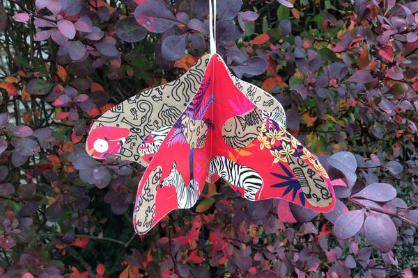 Paper moth decoration hanging in front of purple-leaved bush